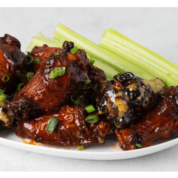 Glazed chicken wings with chopped green onions and celery sticks on a white plate.