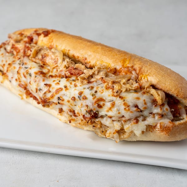 A close-up of a chicken parmesan sub sandwich with melted cheese and herbs on a white plate.