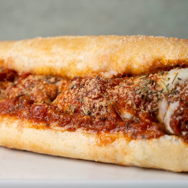 Close-up of a chicken parmesan sub sandwich with red sauce, cheese, and herbs.