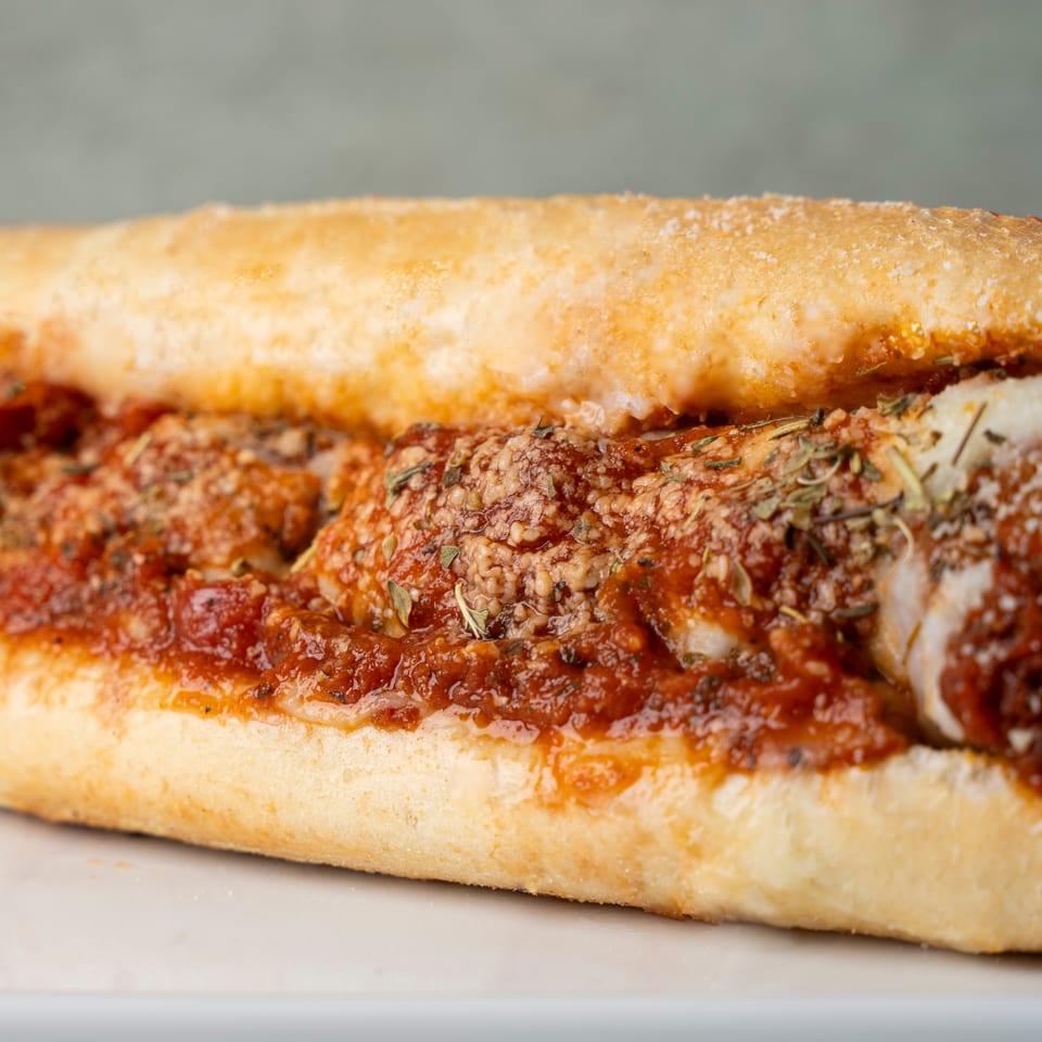 Close-up of a chicken parmesan sub sandwich with red sauce, cheese, and herbs.