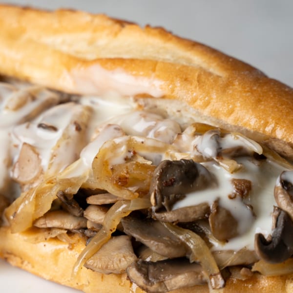 Close-up of a mushroom and onion sub sandwich with creamy white sauce on a baguette.