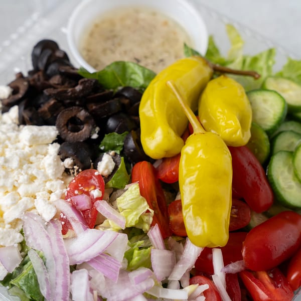Close-up of a vibrant salad with lettuce, tomatoes, cucumbers, olives, feta, onions, and yellow peppers.