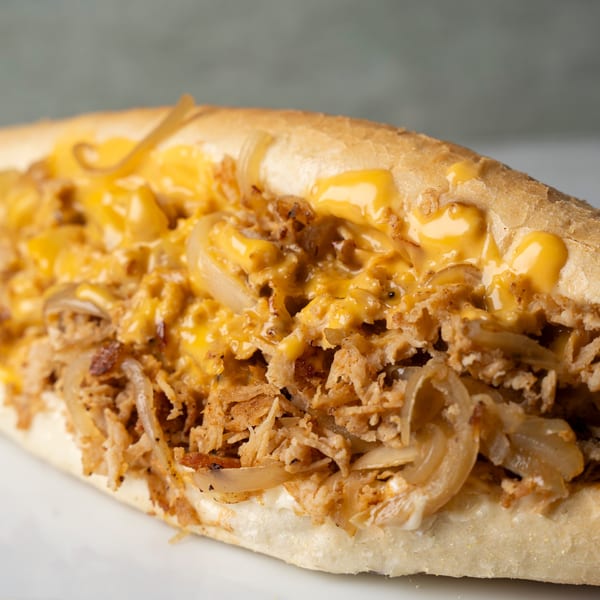 Close-up of a cheesesteak sandwich with melted cheese, shredded meat, and caramelized onions on a hoagie roll.