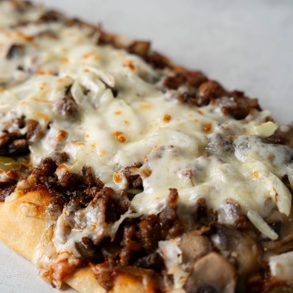 Close-up of a cheesy steak and mushroom flatbread with melted white cheese and browned meat.