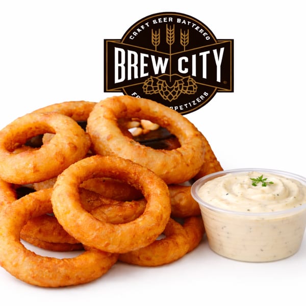 Golden-brown onion rings piled next to a cup of creamy dipping sauce with the Brew City logo.