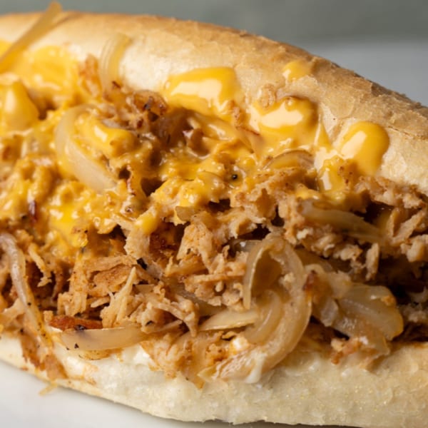 Close-up of a cheesesteak sandwich with shredded meat, onions, and melted cheese sauce.